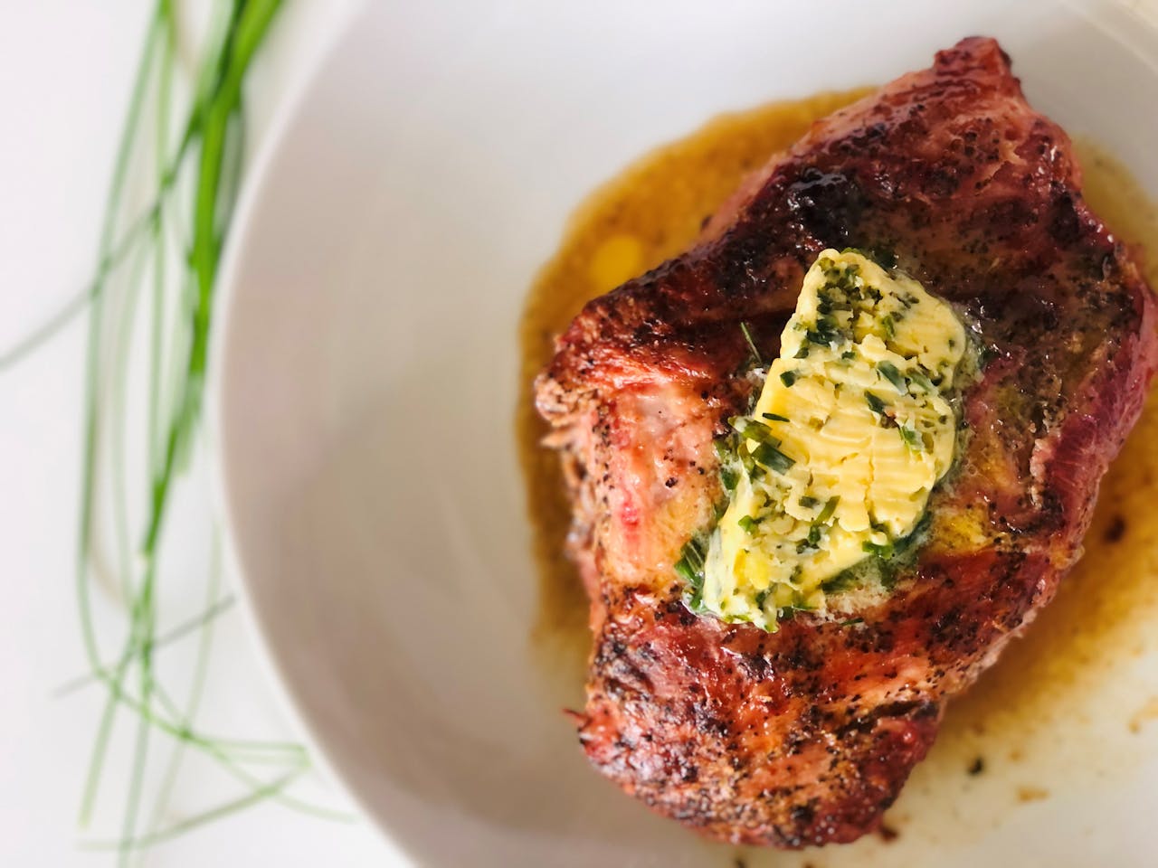 Menus Delicious grilled steak served with a mouthwatering herb butter topping on a white ceramic plate.