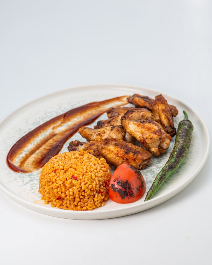 Menus Scrumptious roasted chicken wings with bulgur, green pepper, and tomato on a plate.