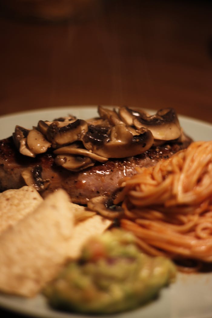 Menus A delicious steak topped with mushrooms, served with pasta and guacamole.